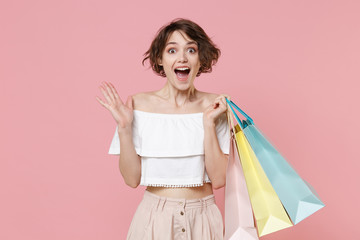 Surprised young woman girl in summer clothes hold package bag with purchases isolated on pastel...
