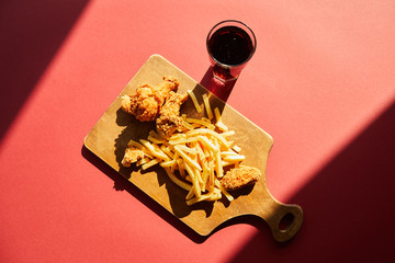 top view of crispy deep fried chicken and french fries served on wooden cutting board with soda in sunlight