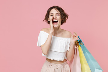 Cheerful young woman girl in summer clothes hold package bag with purchases isolated on pink...