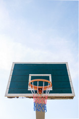 A perspective view of a dark basketball backboard with a multi-colored basketball basket against a bright sky.