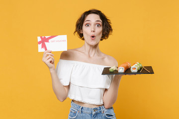 Young woman girl in casual clothes hold in hand gift certificate makizushi sushi roll served on plate traditional japanese food isolated on yellow background studio portrait. People lifestyle concept