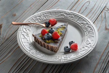 Slice of chocolate cake with nuts, decorated with berries, blueberries and raspberries. With a beautiful golden spoon.