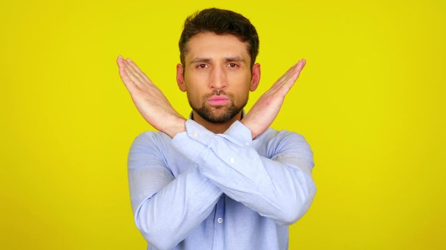 Stop concept: virus, violence, abortion, corruption, inequality, plastic, racism. Serious bearded man in a light blue shirt crossed his arms in front of his chest on yellow background with copy space