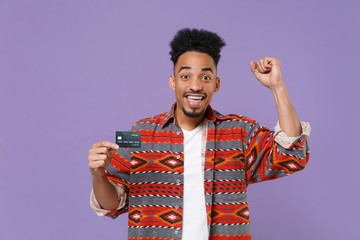 Joyful young african american guy in casual colorful shirt posing isolated on violet wall...