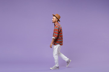 Side view of smiling young african american guy in casual colorful shirt hat posing isolated on...