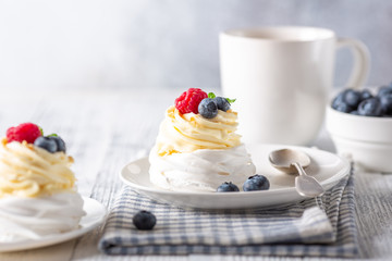 Romantic spring romantic breakfast. Delicious Pavlova cake with cream and fresh berries and mug with coffee. Soft focus