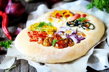 Homemade focaccia with different types of vegetables on a wooden background