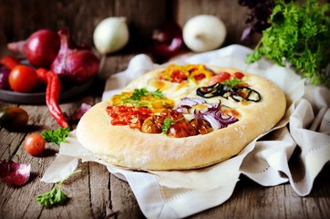 Homemade focaccia with different types of vegetables on a wooden background