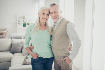 Obraz premium Portrairt of attractive grandparents cuddling looking dressed jeans denim trousers turquoise brown pullovers standing in big room