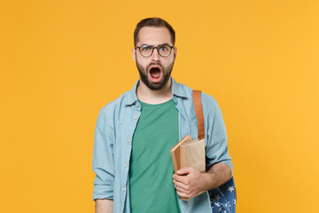 Shocked worried man student in casual clothes glasses backpack hold books isolated on yellow background. Education in high school university college concept. Mock up copy space. Keeping mouth open.