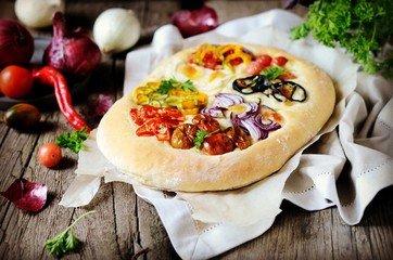 Homemade focaccia with different types of vegetables on a wooden background