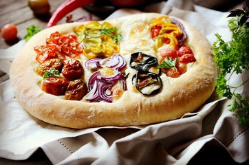 Homemade focaccia with different types of vegetables on a wooden background
