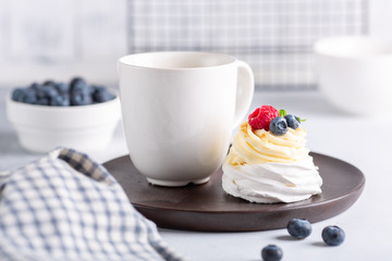 Romantic spring breakfast. Delicious Pavlova cake with cream and fresh berries and mug with coffee. Soft focus