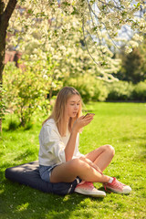 Cute teen girl communicates by voice message on the phone, sitting in the yard of the house, in the garden.