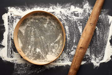white wheat flour scattered on a black table and very old brown wooden rolling pin