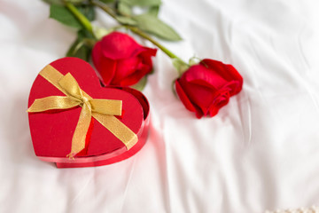 Roses and heart shaped box of candies in bed