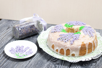 Lavender Cupcake. Sugar coated. Decorated with lavender glaze flowers. Near the bank with lavender inflorescences and a saucer decorated with glaze.