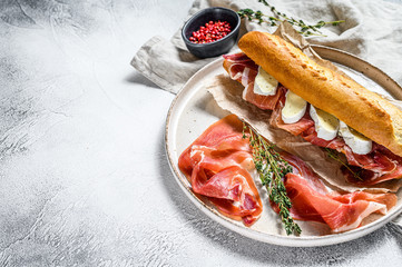 baguette sandwich with jamon ham serrano, paleta iberica, Camembert cheese on the cutting Board.  Gray background, top view, space for text