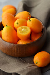Kumquat fruits in wooden bowl on linen background. Healthy vegetarian food.