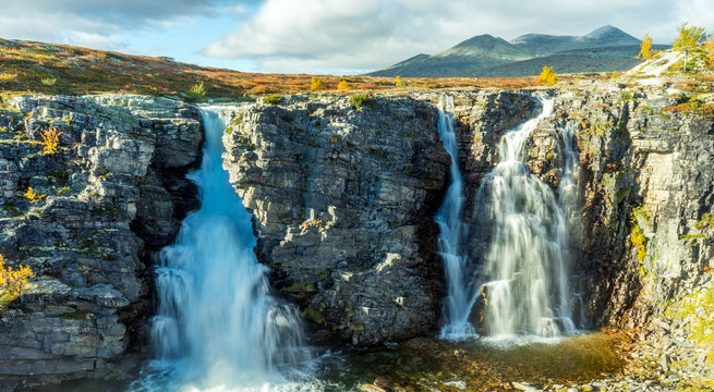 The bridal veil waterfall in Rondane national park in Norway during autumn. Colorful scenery and snow capped mountains in the background.
