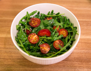 white bowl with healthy salad from arugula and Cherry tomatoes on a wooden  tabletop