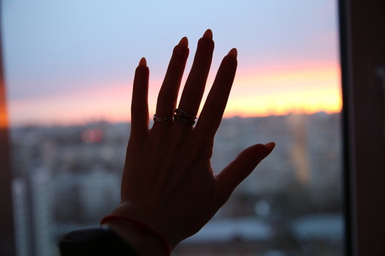 hand of girl with long nails on the background of colourfull sunset. Tired to stay at home. 