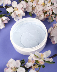Obraz na płótnie Canvas body scrub in a white jar on a purple background with white flowers apple close-up. skin care, cosmetics, beauty, spa