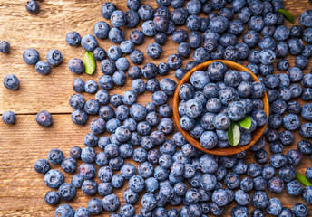 Fresh blueberries with blueberry leaves on wooden background. Top view of bowl with berries.