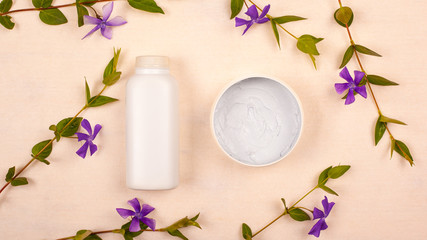Fototapeta na wymiar white jars with cosmetics on a beige background with violet wildflowers top view flat lay. skin care, beauty, skin cleansing