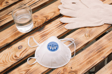 Mask, gloves are lying on the wooden table background. Glass of water is standing on the wooden background. Safety.