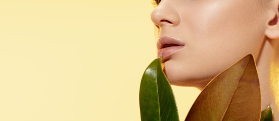Close up of beautiful young woman with green leaves on yellow background. Concept of cosmetics,...