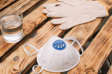 Mask, gloves are lying on the wooden table background. Glass of water is standing on the wooden background. Safety.