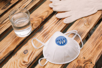 Mask, gloves are lying on the wooden table background. Glass of water is standing on the wooden background. Safety.