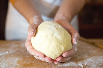Unrecognizable baker holding kneaded dough in palms. Wheat flour on wooden board. Selective focus. Studio shot. Front view. Cooking and baking at home concept