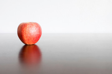 A red apple placed on a wooden table with a white wall background.