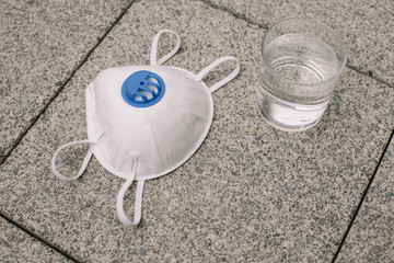 Mask, gloves are lying on the grey table background. Glass of water is standing on the grey background. Safety.