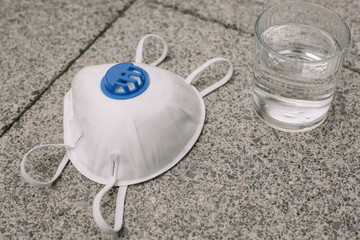 Mask, gloves are lying on the grey table background. Glass of water is standing on the grey background. Safety.