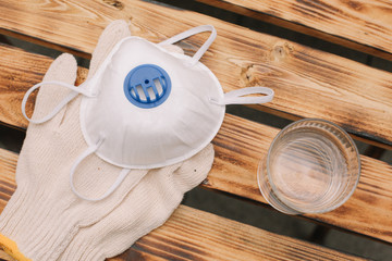 Mask, gloves are lying on the wooden table background. Glass of water is standing on the wooden...