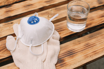 Mask, gloves are lying on the wooden table background. Glass of water is standing on the wooden background. Safety.