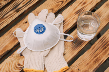 Mask, gloves are lying on the wooden table background. Glass of water is standing on the wooden background. Safety.