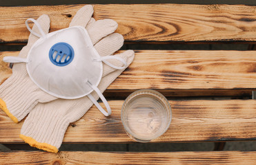 Mask, gloves are lying on the wooden table background. Glass of water is standing on the wooden background. Safety.