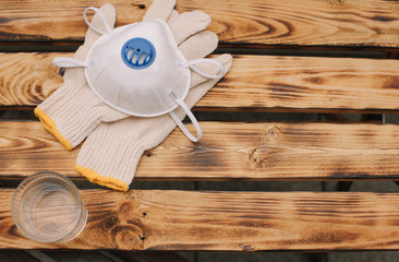 Mask, gloves are lying on the wooden table background. Glass of water is standing on the wooden background. Safety.