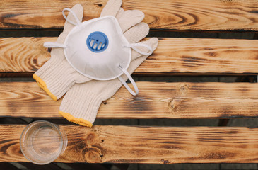 Mask, gloves are lying on the wooden table background. Glass of water is standing on the wooden background. Safety.