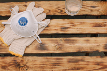 Mask, gloves are lying on the wooden table background. Glass of water is standing on the wooden background. Safety.