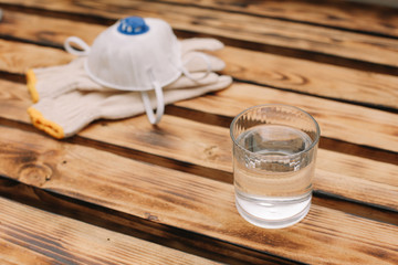 Mask, gloves are lying on the wooden table background. Glass of water is standing on the wooden background. Safety.