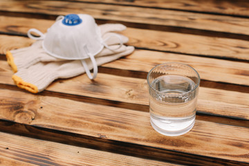 Mask, gloves are lying on the wooden table background. Glass of water is standing on the wooden background. Safety.