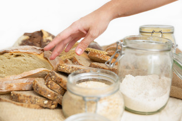 Female hand of reaching wholegrain toast in heap of freshly baked loafs. Closeup shot, side view. Traditional bread or bakery concept