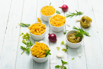 uncooked pasta variations and fresh spices on white wooden table