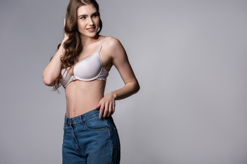 happy girl in bra and denim jeans standing on grey
