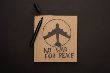 top view of cardboard placard with no war for peace lettering and plane near marker on black background